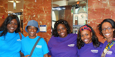 A group of women smile and link arms together