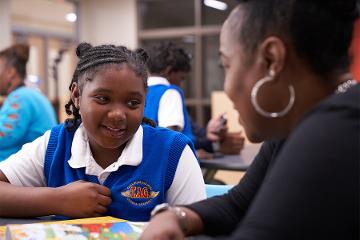 a girl wearing a blue vest smiles at a woman