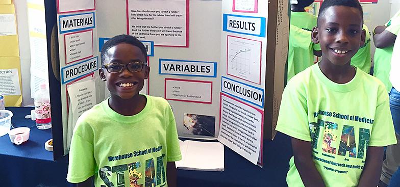 Younger students smiling in front of a poster