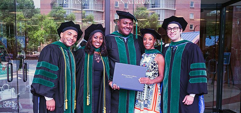 A group of students in commencement regalia holding a diploma 