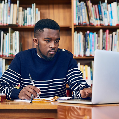 a man studies using a laptop on a library table 