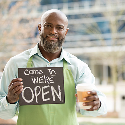 a man in an apron holds a sign 'come in we're open'